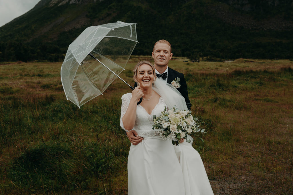 Wedding couple smiling at the camera in the rain under an umbrella