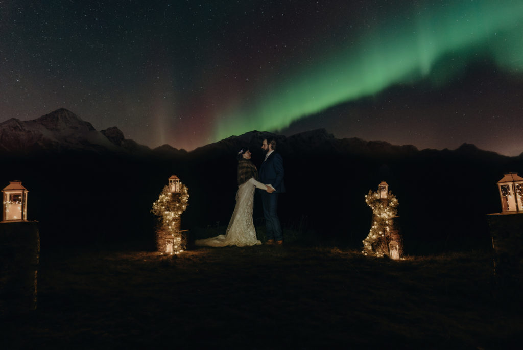 wedding couple holding hands under the northern lights dancing on the sky in norway