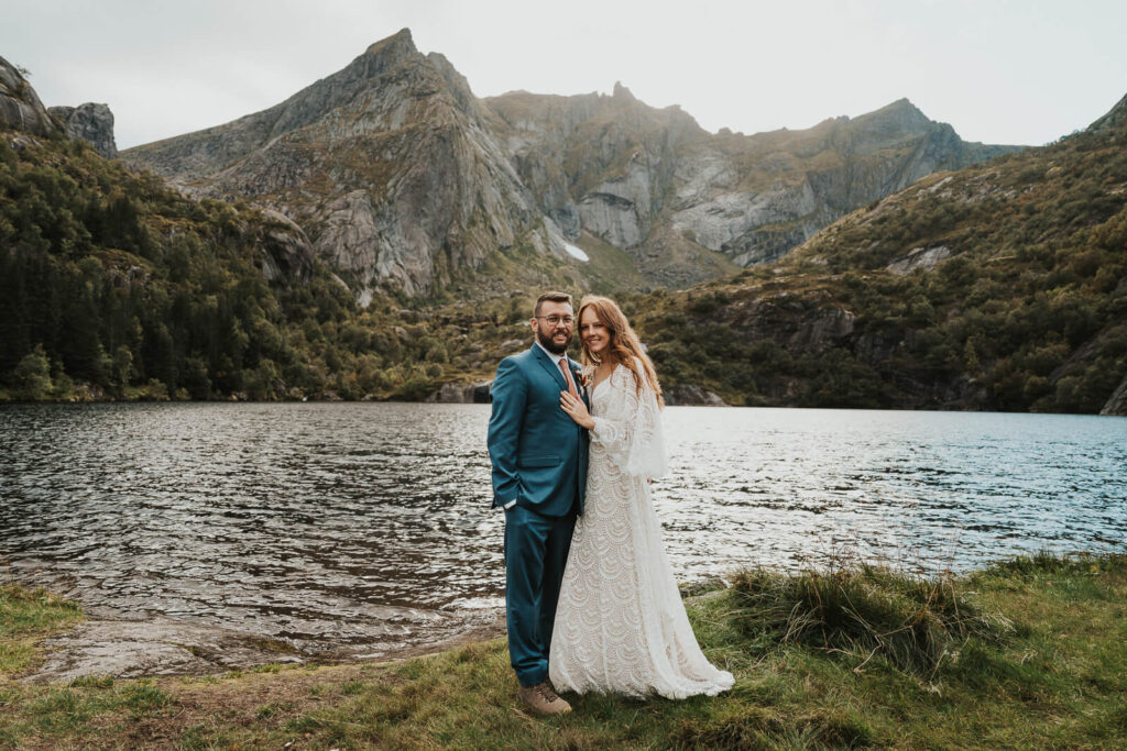 Elopement couple smiling at the camera with a huge mountain in the background in Lofoten Norway