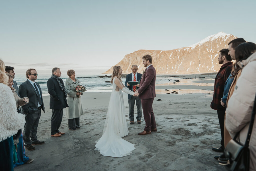 Wedding couple holding hands during their wedding ceremony on a beach in Lofoten