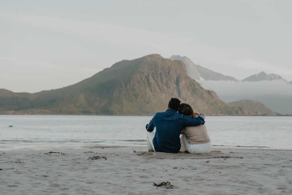 Couple sitting on a beach in Lofoten looking out over the ocean